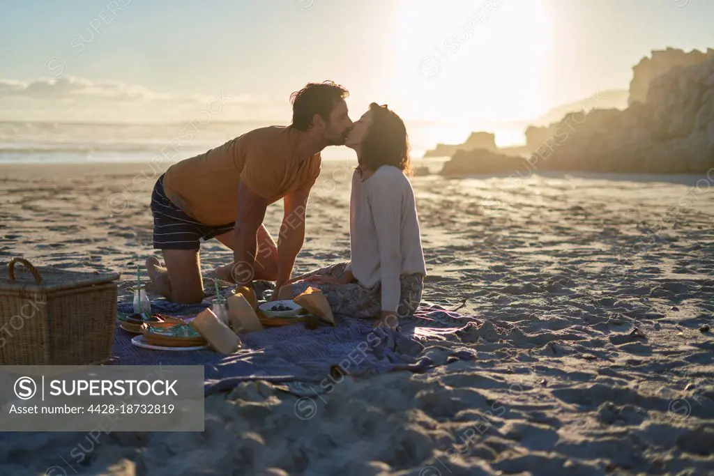 Affectionate couple kissing on picnic blanket on sunny summer beach