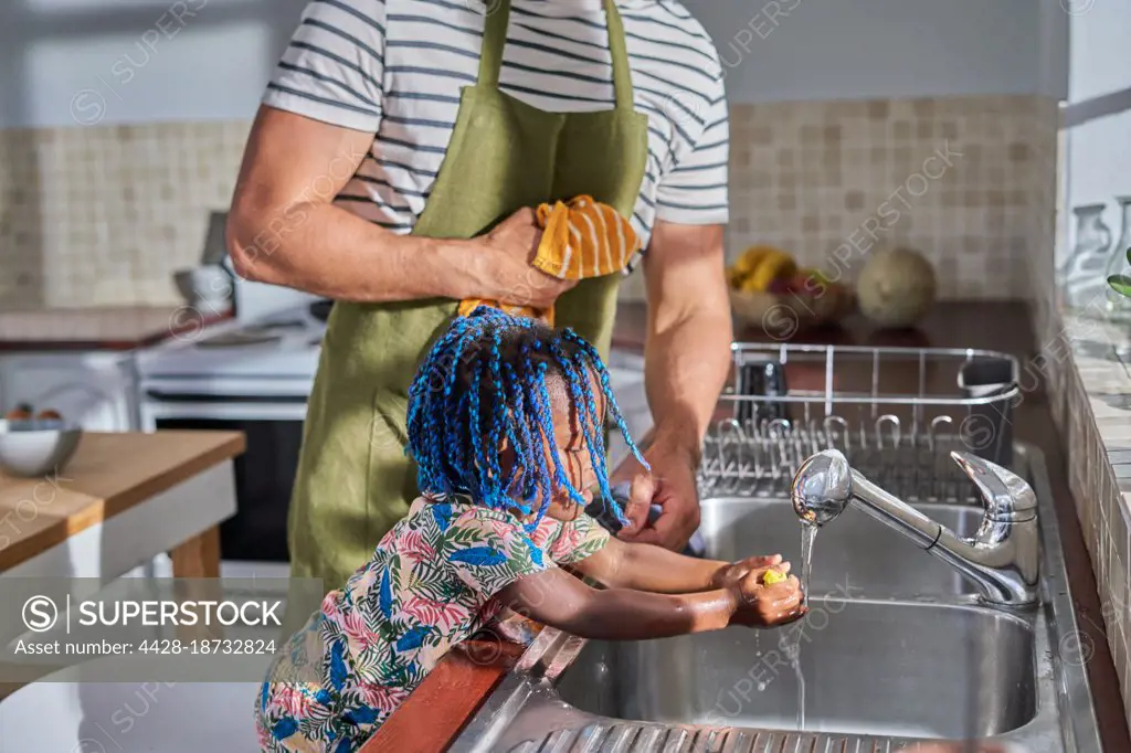 Father and toddler daughter washing hands at kitchen sink