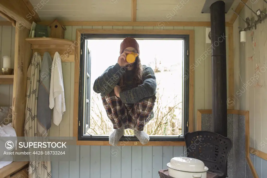 Young man in pajamas drinking coffee in tiny cabin window