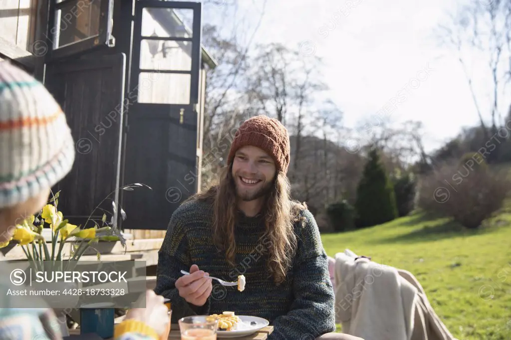 Happy young man eating breakfast outside tiny cabin rental