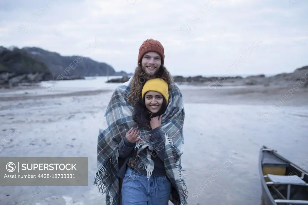 Portrait happy young couple wrapped in a blanket on beach