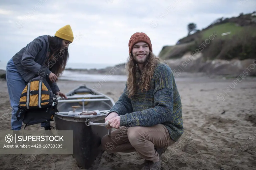 Smiling young couple with canoe on beach