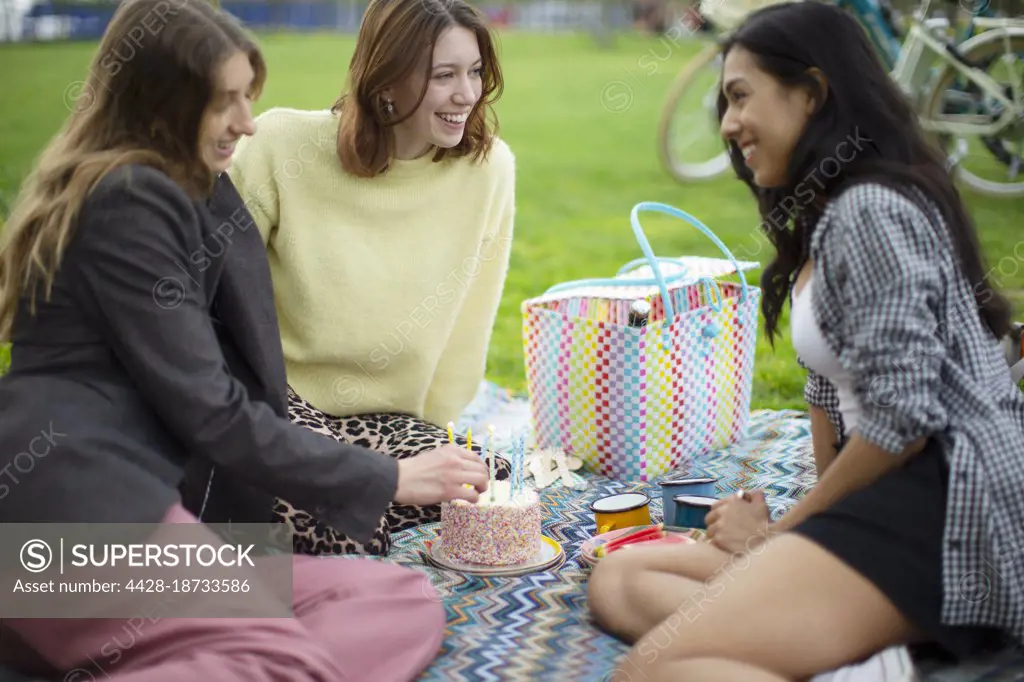 Happy young women friends celebrating birthday with cake in park