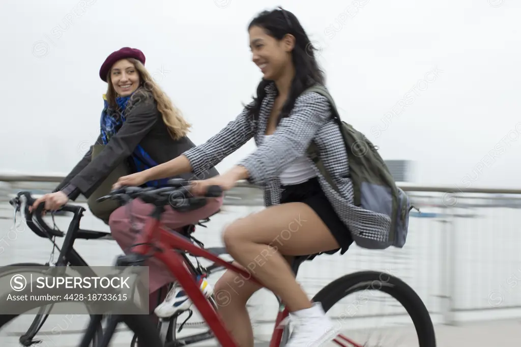 Happy young women friends riding bicycles on bridge