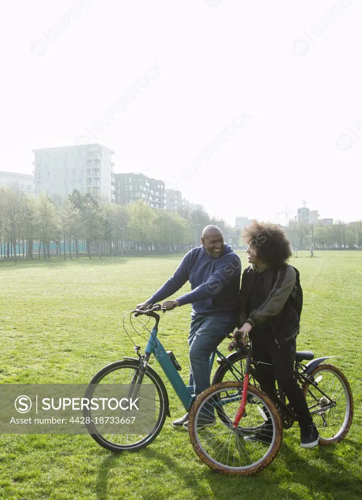 Father and son riding bicycles in sunny urban park
