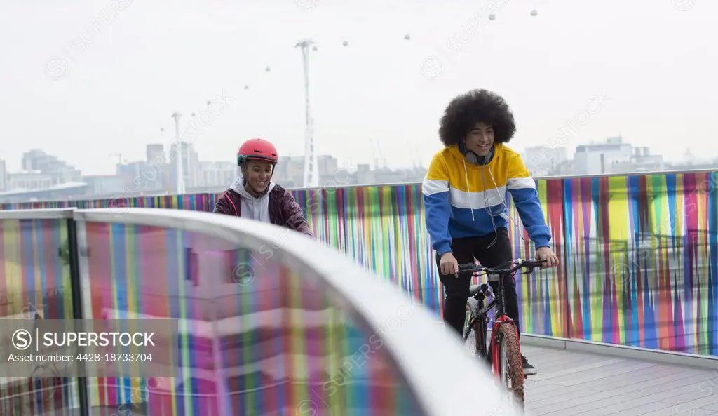 Teen friends riding bicycles on modern footbridge in city, London, UK