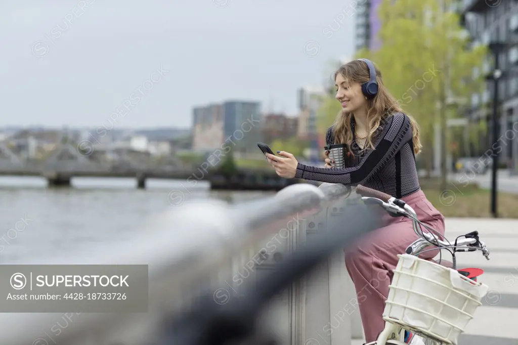 Young woman with headphones using smart phone at urban waterfront