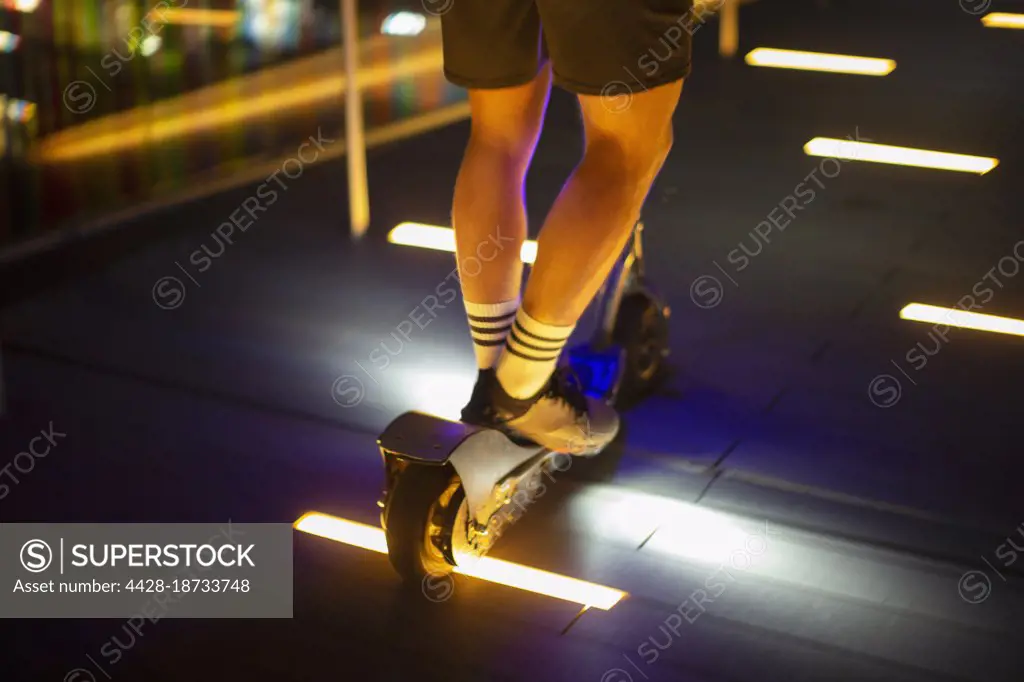Man riding scooter on illuminated sidewalk at night