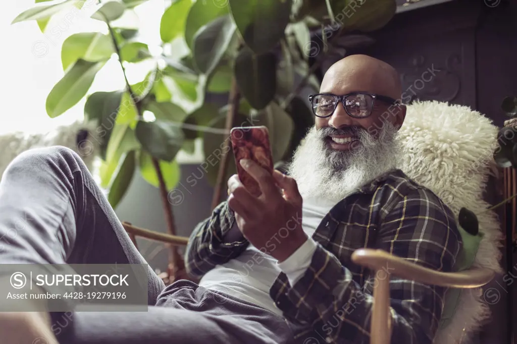 Happy senior man using smart phone in armchair