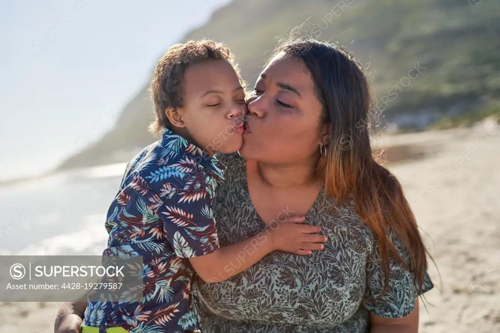 Happy, affectionate mother and son kissing on sunny beach