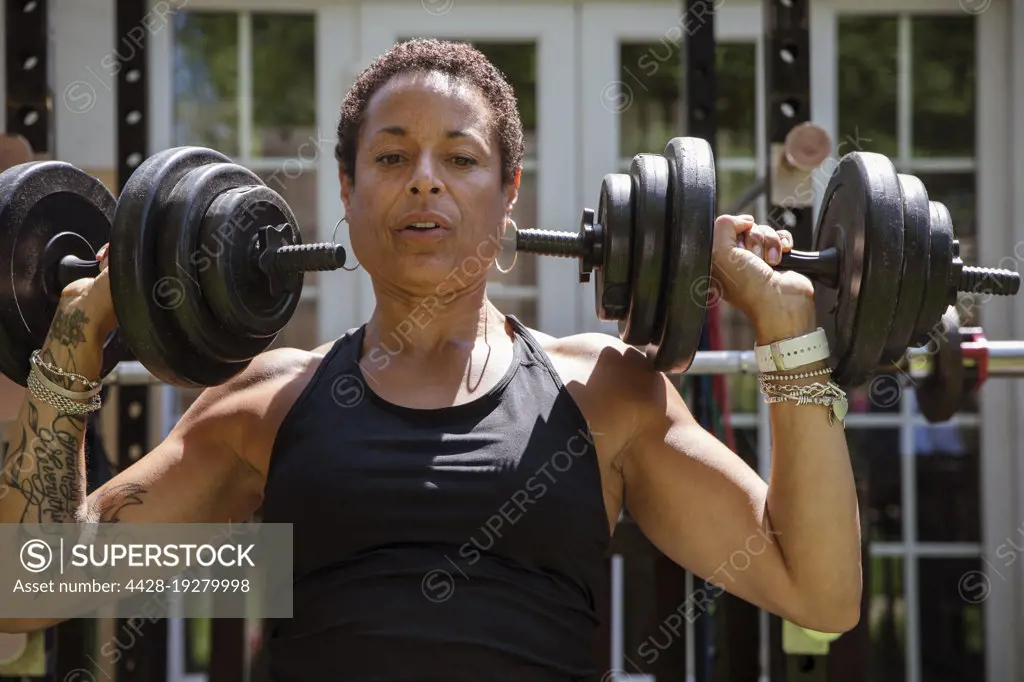 Strong mature woman weightlifting in sunny backyard