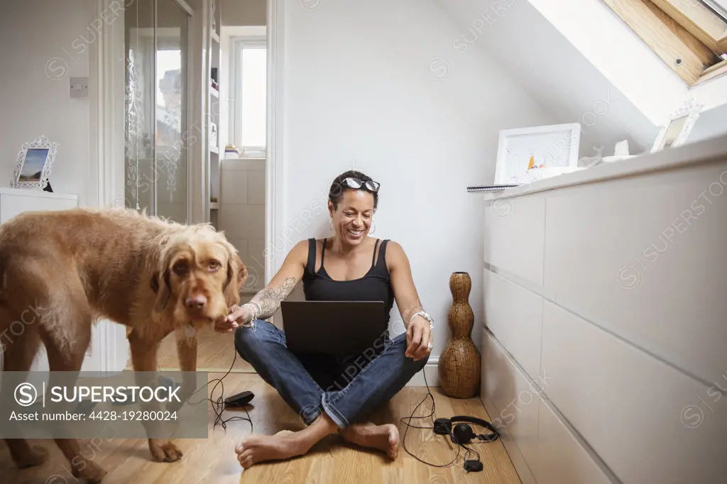 Happy woman with dog and laptop on bedroom floor