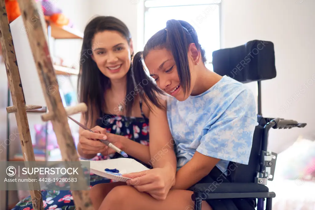 Happy mother and disabled daughter in wheelchair painting at home