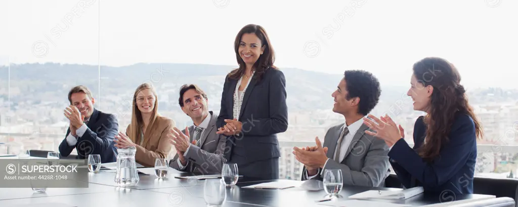 Spain, Co-workers clapping for businesswoman in conference room