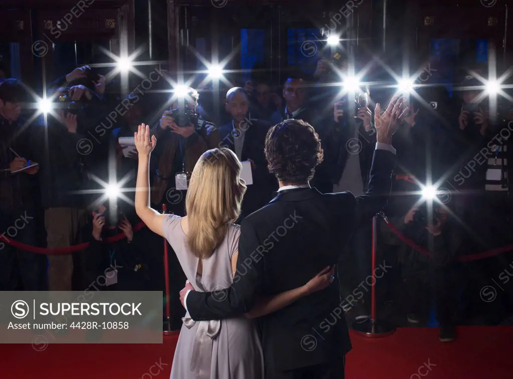 Rear view of celebrity couple waving to paparazzi at red carpet event