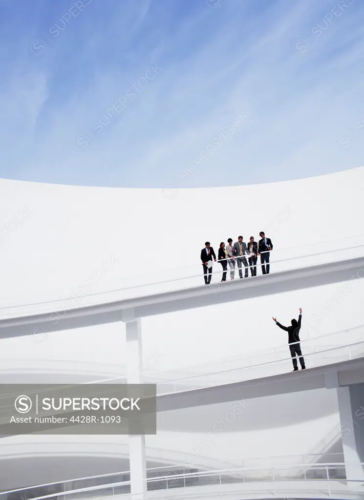 Spain, Business people looking down at businessman with arms raised on elevated walkway