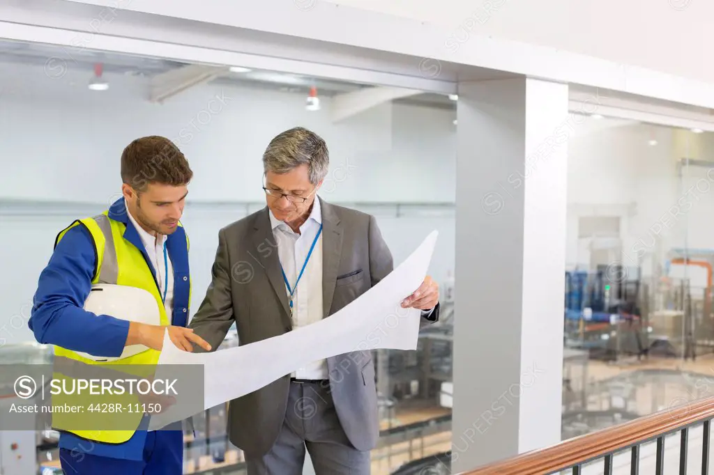 Supervisor and worker reading blueprints in factory