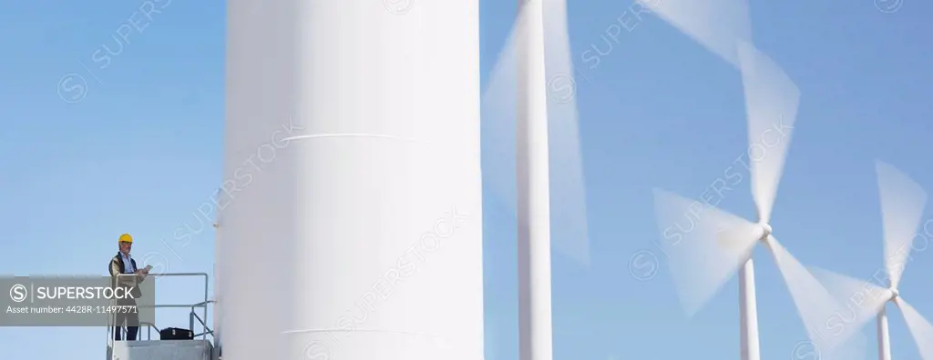 Worker standing on wind turbine in rural landscape
