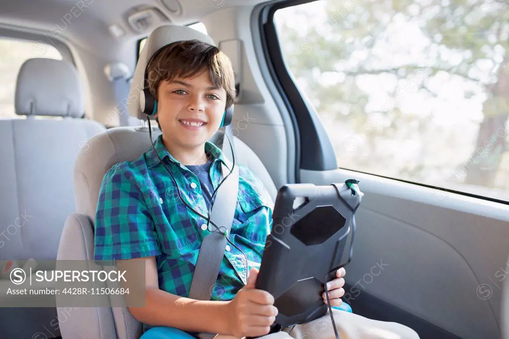 Portrait of happy boy with headphones using digital tablet in back seat of car