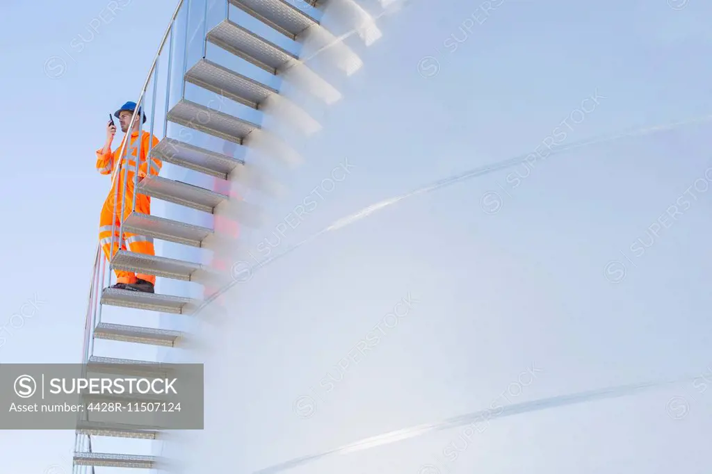 Worker using walkie-talkie on stairs along silage storage tower