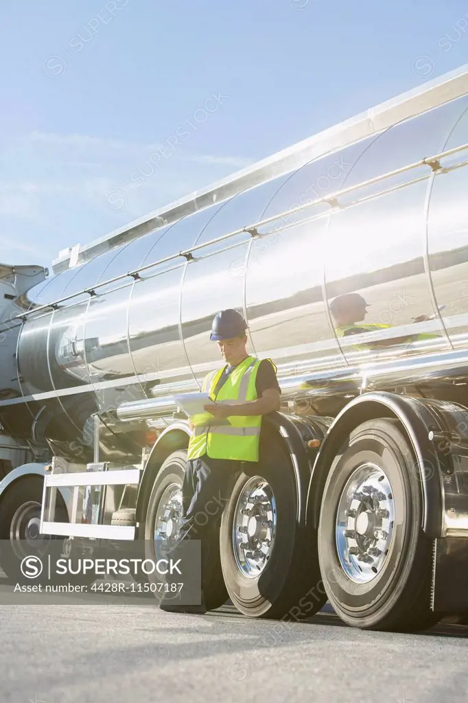 Worker with clipboard leaning on stainless steel milk tanker