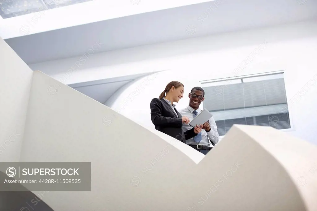 Businessman and businesswoman using digital tablet on modern staircase