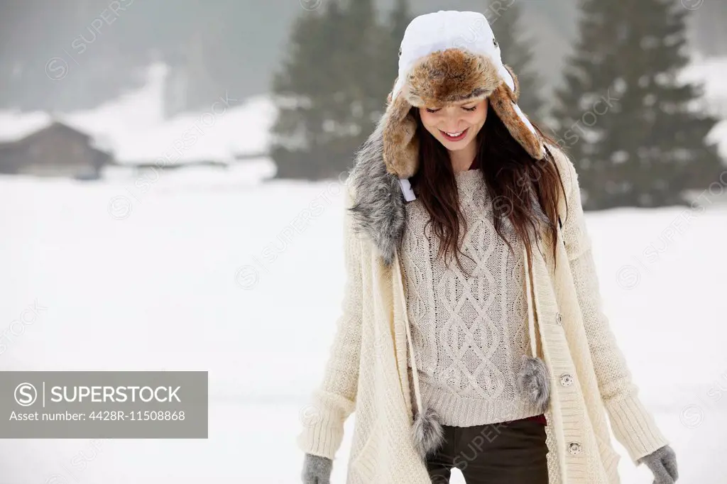 Smiling woman wearing fur hat in snowy field