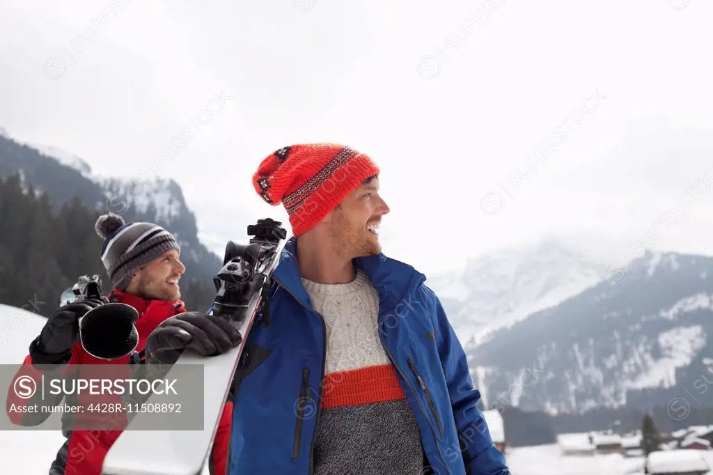 Smiling men carrying skis at base of mountain