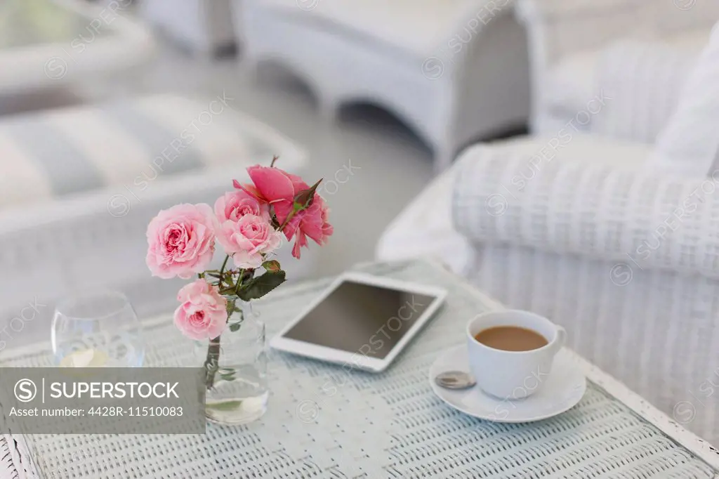 Pink roses on patio table with coffee cup and digital tablet
