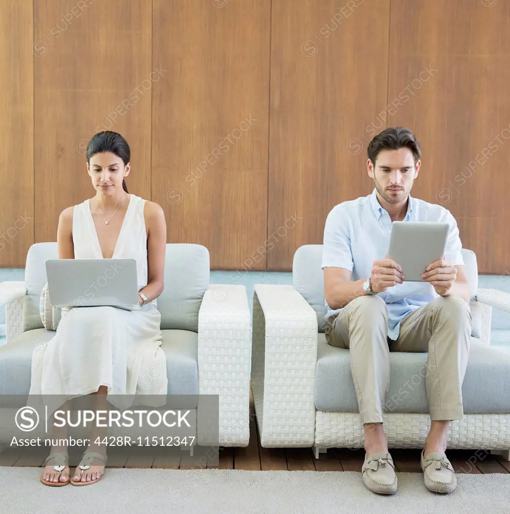 Couple using digital tablet and laptop in armchairs