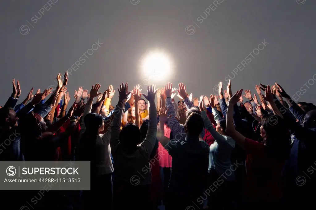 Diverse crowd with arms raised around bright light