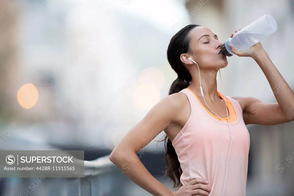 Woman drinking water after exercising on city street