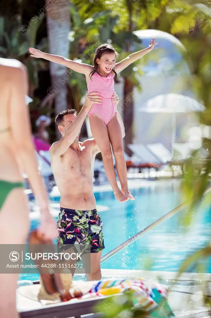 Father lifting smiling daughter by swimming pool