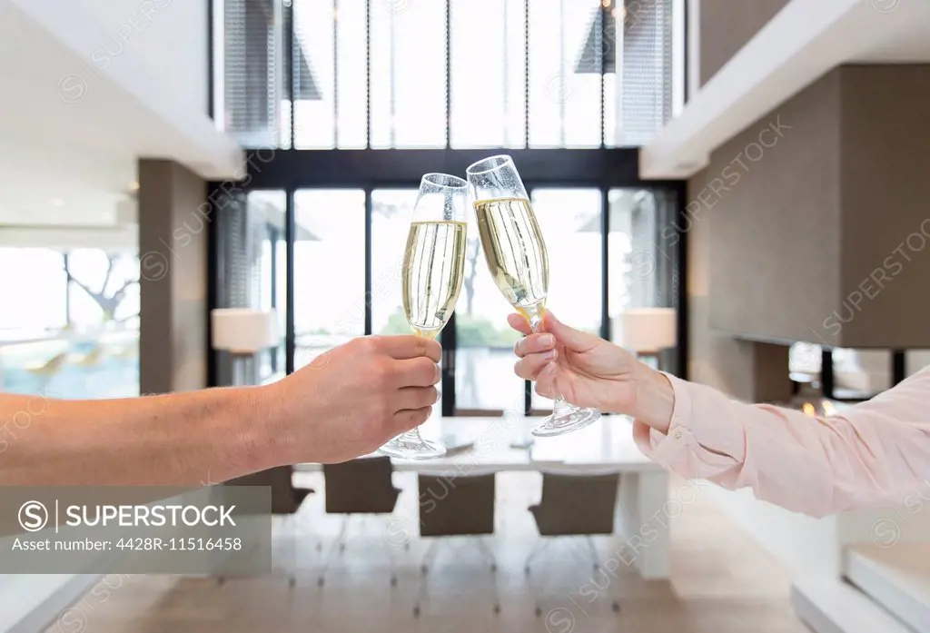 Hands of couple raising toast with champagne flutes in modern dining room