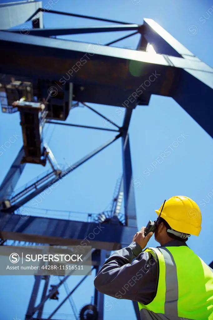 Low angle view of worker using walkie-talkie near crane