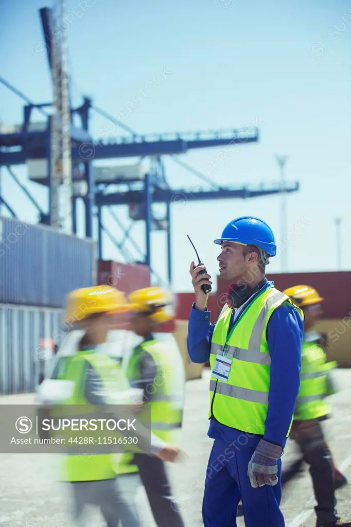 Worker using walkie-talkie near cargo containers