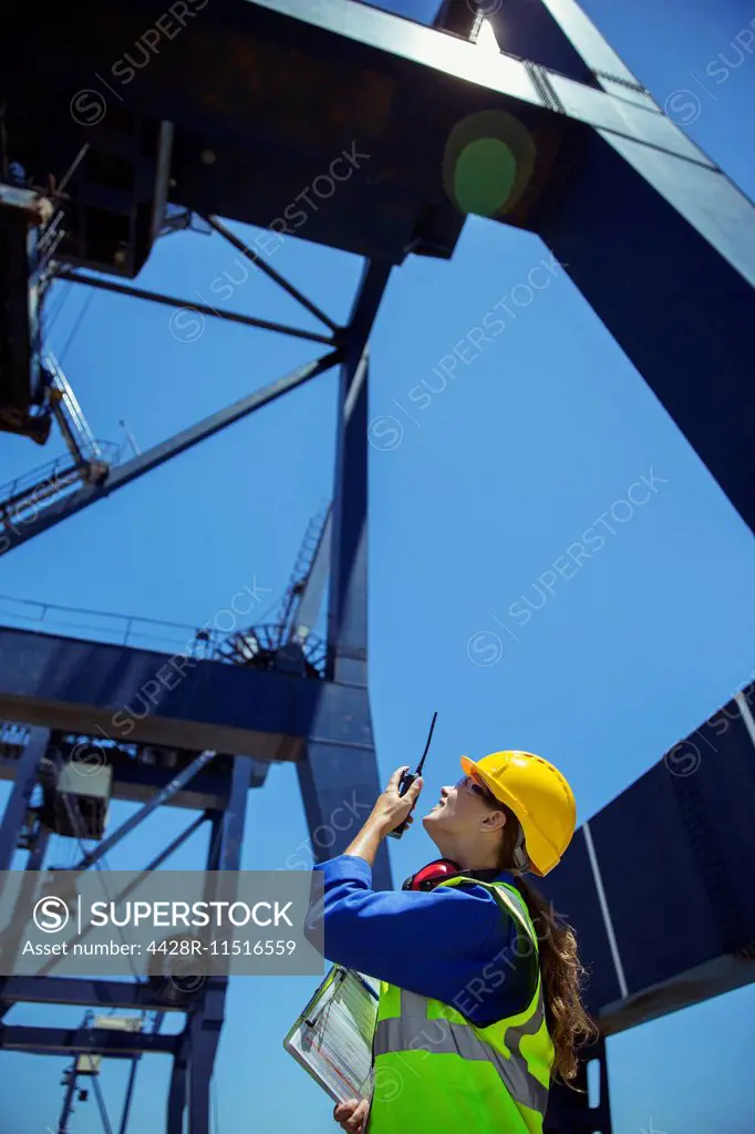 Low angle view of worker using walkie-talkie under cargo crane