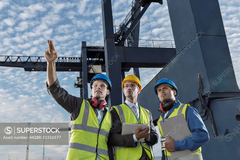 Businessmen and worker talking near cargo crane