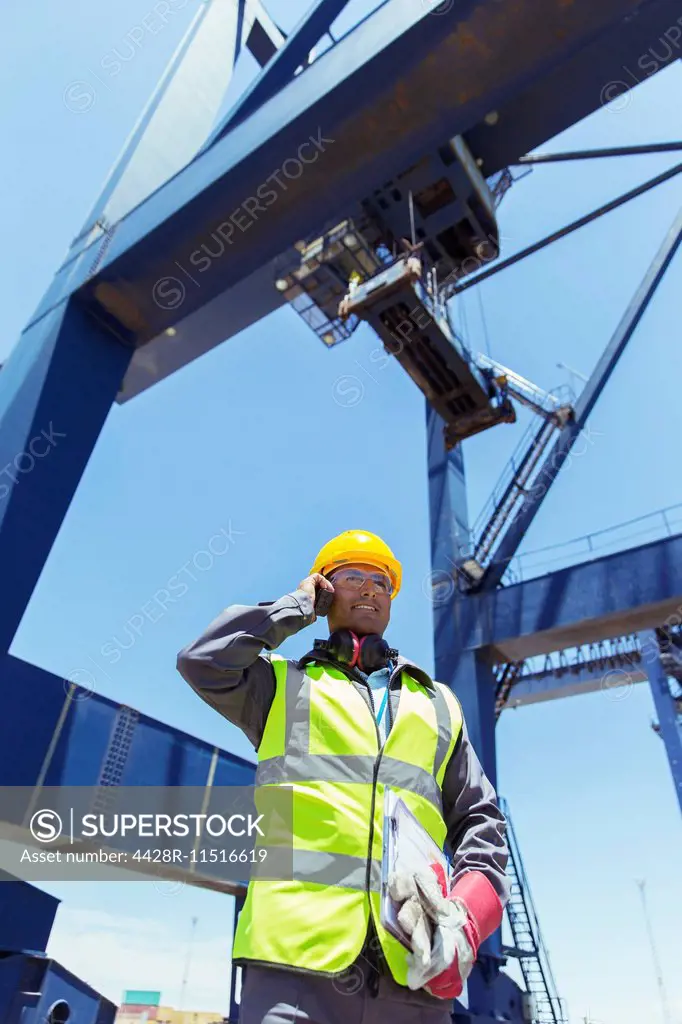 Low angle view of worker talking on walkie-talkie under cargo crane
