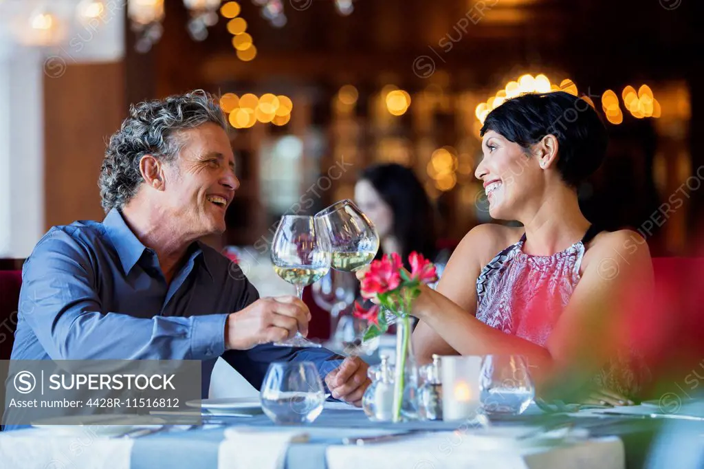 Smiling mature couple raising toast with white wine at restaurant table