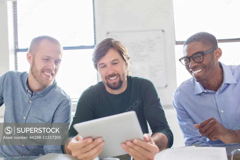 Three smiling men working with digital tablet in office