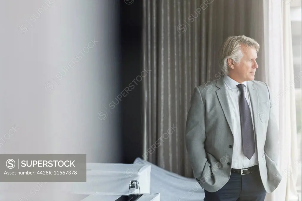 Portrait of businessman with hands in pockets standing in conference room, looking out of window