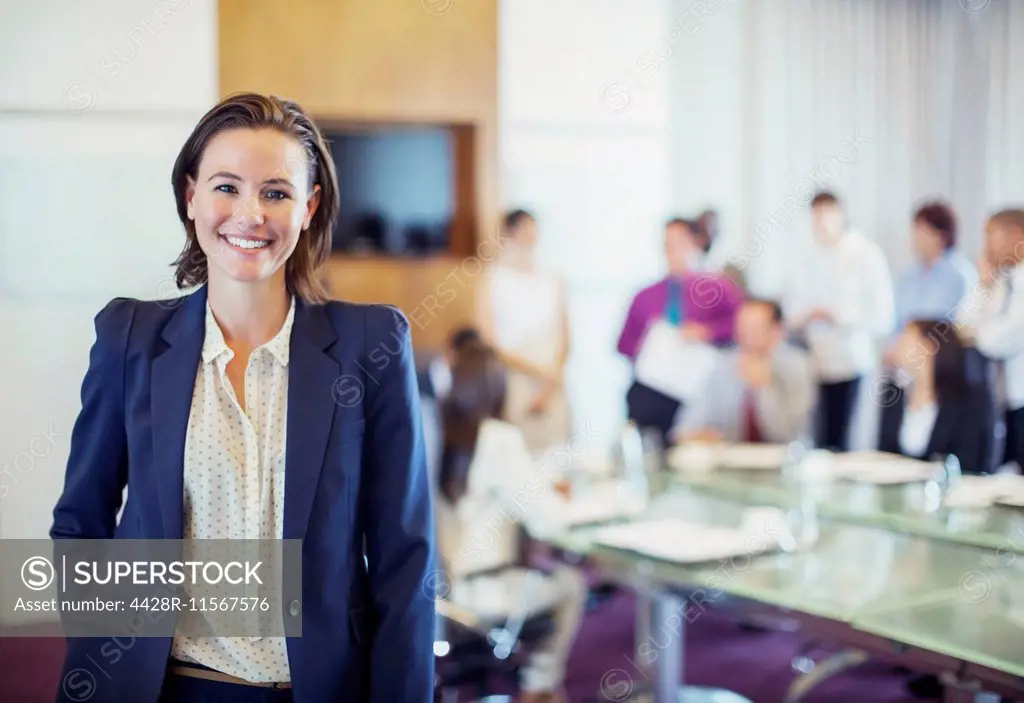 Portrait of young businesswoman smiling in conference room, people in background
