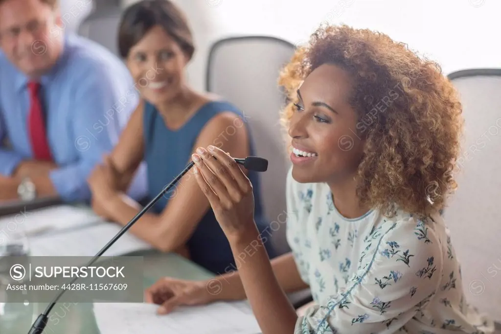 Beautiful woman sitting at conference table talking into microphone