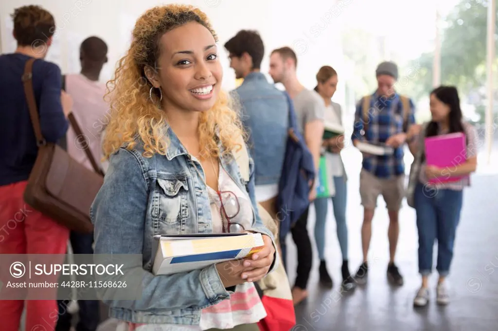 Smiling female student holding books and looking at camera