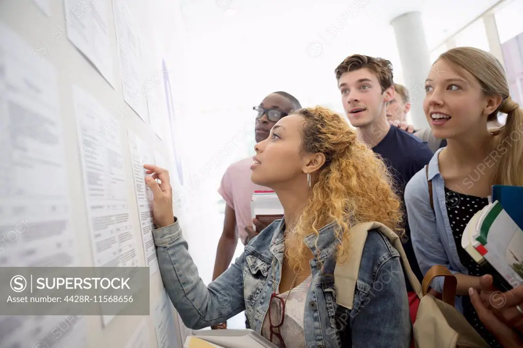 Group of students looking at information board and holding books at school