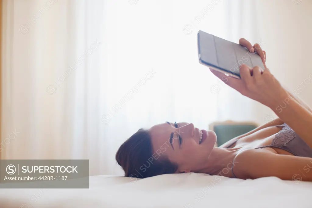 Venice, Smiling woman laying on bed and using digital tablet