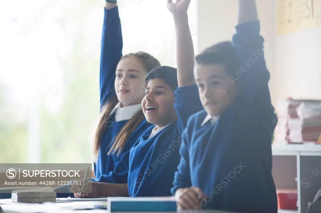 Primary school children in classroom raising arms