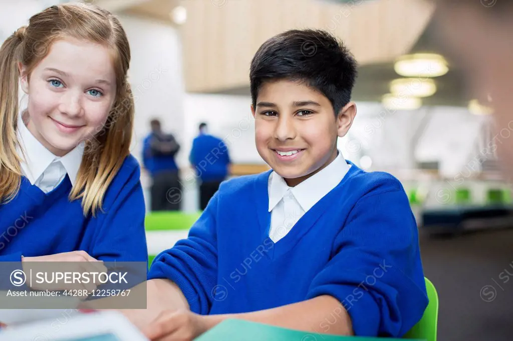 Portrait of smiling school children wearing blue school uniforms sitting at desk