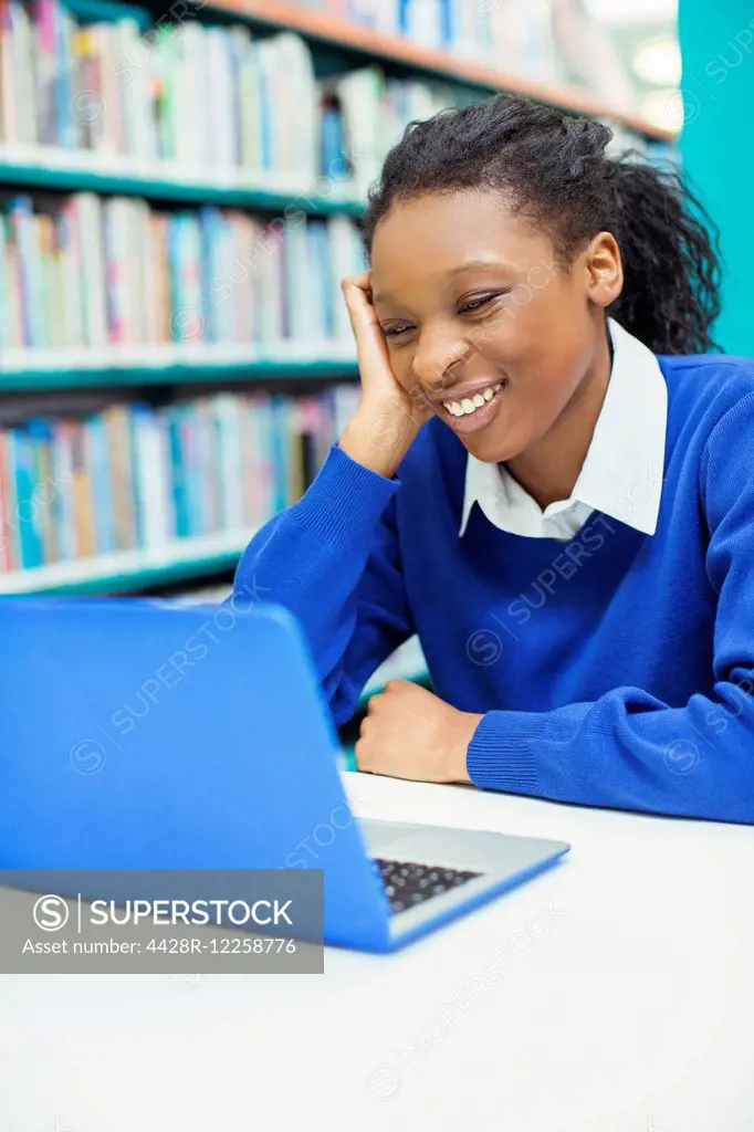 Smiling female student looking at laptop in library